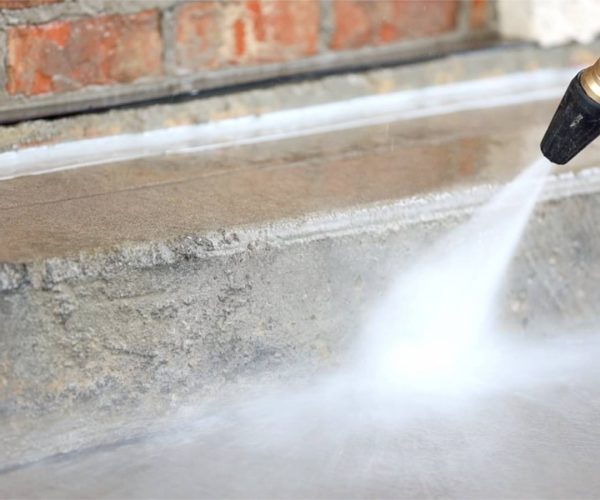 cleaning professional with sprayer cleaning concrete in front of brick building